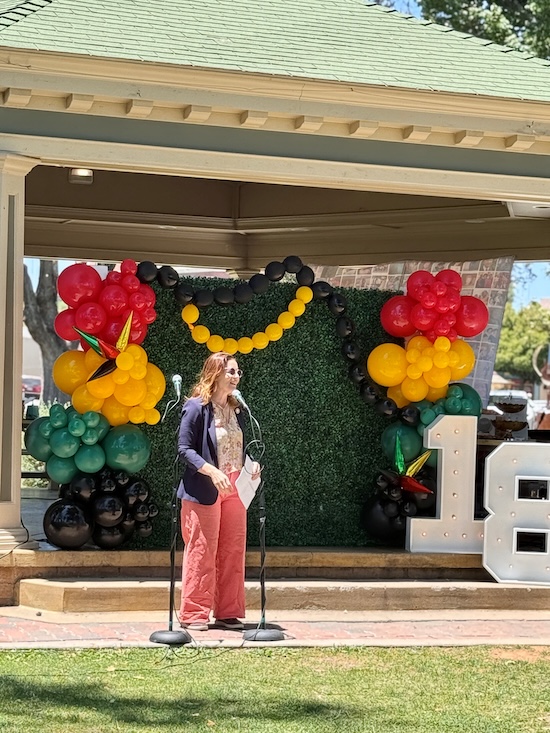 Asm Addis addressing the attendees in the park with a gazebo behind me, along with red, yellow, green and black balloons