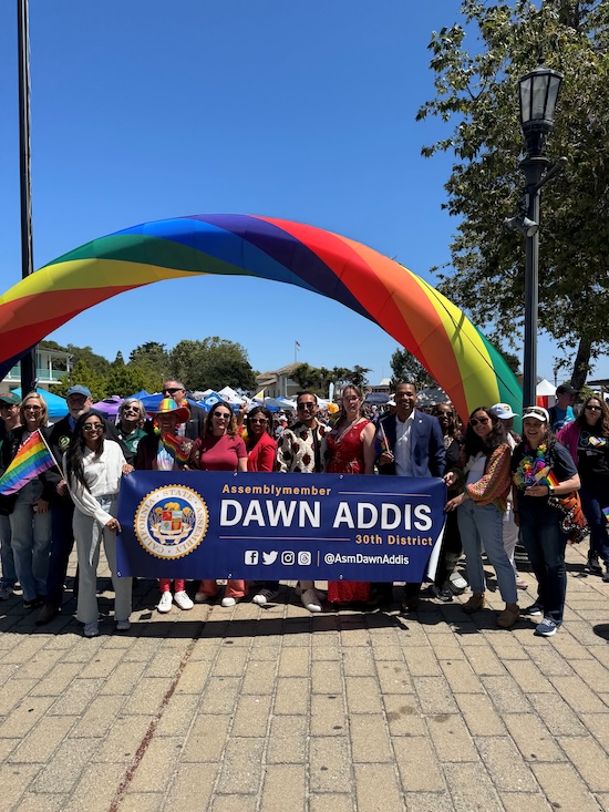 Asm Addis at Monterey Peninsula Pride standing under a rainbow arch with members of our community