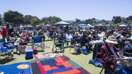 Large audience in grassy area, sitting on lawn chairs