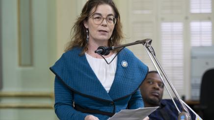 Asm. Addis on the Assembly Floor, speaking into microphone and holding papers