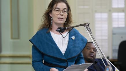 Asm. Addis on the Assembly Floor, speaking into microphone and holding papers