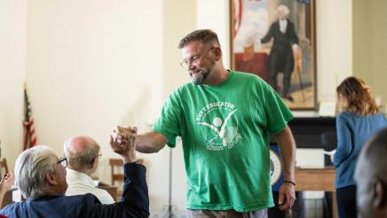 Guest speaker clasps hands with seated attendee