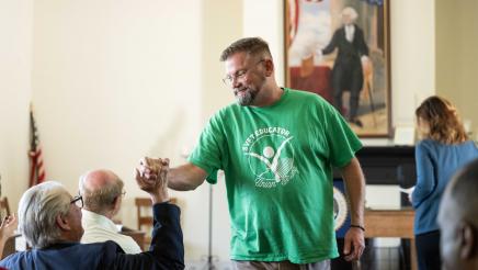 Guest speaker clasps hands with seated attendee