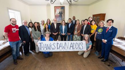 Group photo of Asm. Addis, Speaker Rivas and multiple attendees, some holding a long banner