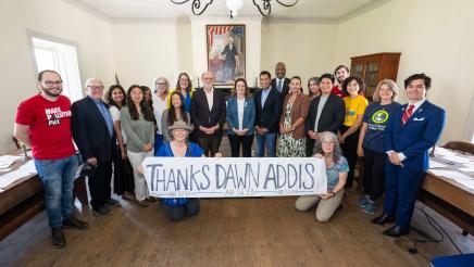 Group photo of Asm. Addis, Speaker Rivas and multiple attendees, some holding a long banner