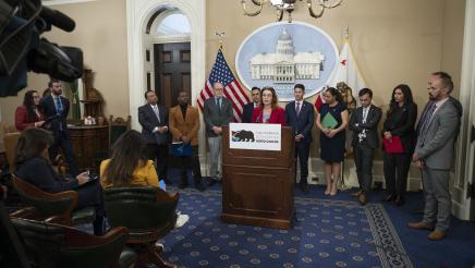 Asm. Addis at podium, speaking, with caucus members standing in background