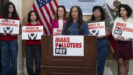 Jessica Calix at podium, speaking, as Asm. Addis and others listen on