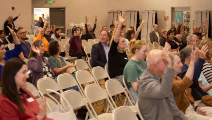 Many seated audiencemembers raising hands
