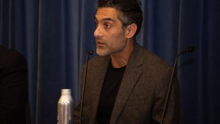 Guest speaker seated at table, speaking into microphone