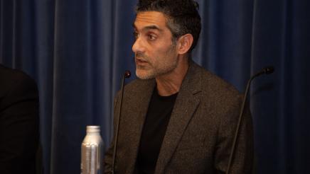 Guest speaker seated at table, speaking into microphone