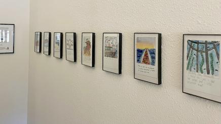 Multiple framed paintings with captions hanging on wall